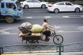 An elderly woman riding a tricycle and pulling the acquired waste goods on the road