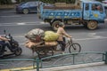 An elderly woman riding a tricycle and pulling the acquired waste goods on the road