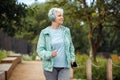 An elderly woman with a short haircut dressed in sportswear is jogging in the park while listening to music. Royalty Free Stock Photo