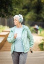 An elderly woman with a short haircut dressed in sportswear is jogging in the park while listening to music. Royalty Free Stock Photo