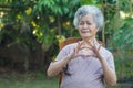 Elderly woman with short white hair sitting smiling and trying make heart symbol by fingers