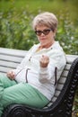 An elderly woman sitting on bench and threatens with fist