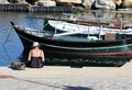 Elderly woman sitting on the pier. Boats in the background.