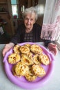 Elderly woman sitting at a table with a cakes - karelian pasty. Happy.