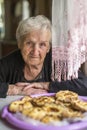 An elderly woman sitting at a table with a Karelian pasty. Tradition.