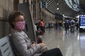 Elderly woman sitting waiting in face mask inside station