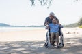 Elderly woman sitting in wheelchair and husband is a wheelchair user smartphone taking selfie on the beach