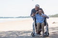 Elderly woman sitting in wheelchair and husband is a wheelchair user smartphone taking selfie on the beach