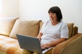 Elderly woman smiling 60s, sitting at home on couch, holding laptop. Senior Royalty Free Stock Photo