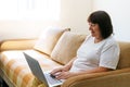 Elderly woman smiling 60s, sitting at home on couch, holding laptop. Senior Royalty Free Stock Photo