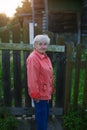 An elderly woman stand near the fence of a village house. Royalty Free Stock Photo