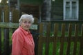 An elderly woman stand near the fence of a village house. Royalty Free Stock Photo