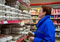 An elderly woman is standing by the shelves with chicken eggs in the grocery store