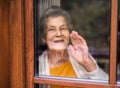 An elderly woman standing by the window, looking out. Shot through glass.