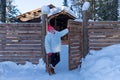 Elderly woman stands near the gate near a wooden house among the snowdrifts in the forest Royalty Free Stock Photo