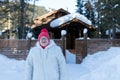 Elderly woman stands and smiles happily in front of a rustic wooden house among the snowdrifts in the forest Royalty Free Stock Photo
