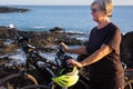 An elderly woman stops on the cliff with her e bike. Two electric bicycle close to her. Blue sea water on background. Sunset light Royalty Free Stock Photo