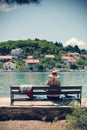 Elderly woman with straw hat sitting on bench by the sea and enjoying the view Royalty Free Stock Photo