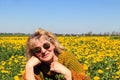 An elderly woman in sunglasses in a meadow with yellow dandelions, close-up-the concept of pleasant spring walks in nature