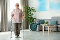 Elderly woman using walking frame indoors. for text