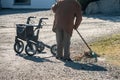 Elderly woman with walker, rakes the lawn and doing gardening work