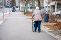 Elderly woman walking with a wheeled walker on an empty street in autumn
