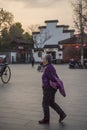 An elderly woman walks past Confucius temple square in the evening.