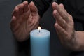 An elderly woman warms her hands with fire from a candle, selective focus. Concept: shutdowns of heating and electricity, rising