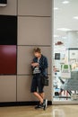 Elderly woman wearing casual clothes and holding smartphone in hand at the shopping centre. Active old age concept