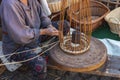 An elderly woman weaves a basket by hand.