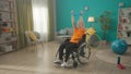 An elderly woman in a wheelchair is exercising with a sports elastic band in the living room. An elderly grayhaired