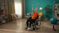 An elderly woman in a wheelchair is exercising with a sports elastic band in the living room. An elderly grayhaired