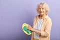 Elderly woman wiping plate and looking at the camera isolated on violet.