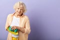 Elderly woman wiping plate and looking at the camera isolated on violet.