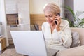 Elderly woman working on laptop computer, smiling, talking on the phone. Senior woman using laptop. Elderly woman sitting at home Royalty Free Stock Photo