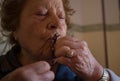 Elderly woman 70-80 years old prays with the rosary at home and she kisses the cross with closed eyes