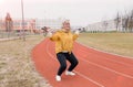 An elderly woman in a yellow sports jacket does physical exercises with Nordic sticks in her hands at the stadium Royalty Free Stock Photo