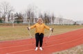 An elderly woman in a yellow sports jacket does physical exercises with Nordic sticks in her hands at the stadium Royalty Free Stock Photo