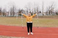 An elderly woman in a yellow sports jacket does physical exercises with Nordic sticks in her hands at the stadium Royalty Free Stock Photo