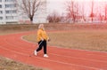 An elderly woman in a yellow sports jacket practices Nordic walking outdoors on the stadium`s rubber treadmill. A sunny sunset.