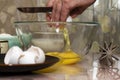 An elderly woman breaks an egg with a knife into a glass bowl for making pancake batter.Ingredients on the table-milk, salt, sugar Royalty Free Stock Photo
