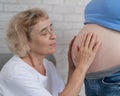 An elderly woman leans against the belly of her pregnant daughter. Close-up.