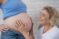 An elderly woman leans against the belly of her pregnant daughter. Close-up.