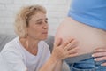 An elderly woman leans against the belly of her pregnant daughter. Close-up.