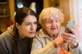 Elderly woman looks and typing on a smartphone, with his adult girl granddaughter. Family. Royalty Free Stock Photo