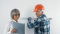 An elderly worker in a hard hat and a gray-haired female engineer with a tablet in their hands are discussing plans Royalty Free Stock Photo