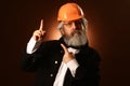 An elderly worker in a helmet gestures warning signs, studio portrait