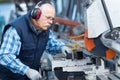 Elderly worker watches processing detail on milling machine