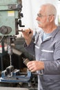 Elderly worker watches processing detail on milling machine