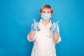 Eldery caucasian doctor lady in white coat and with stethoscope on blue background. Emotional portraits, making thumbs up